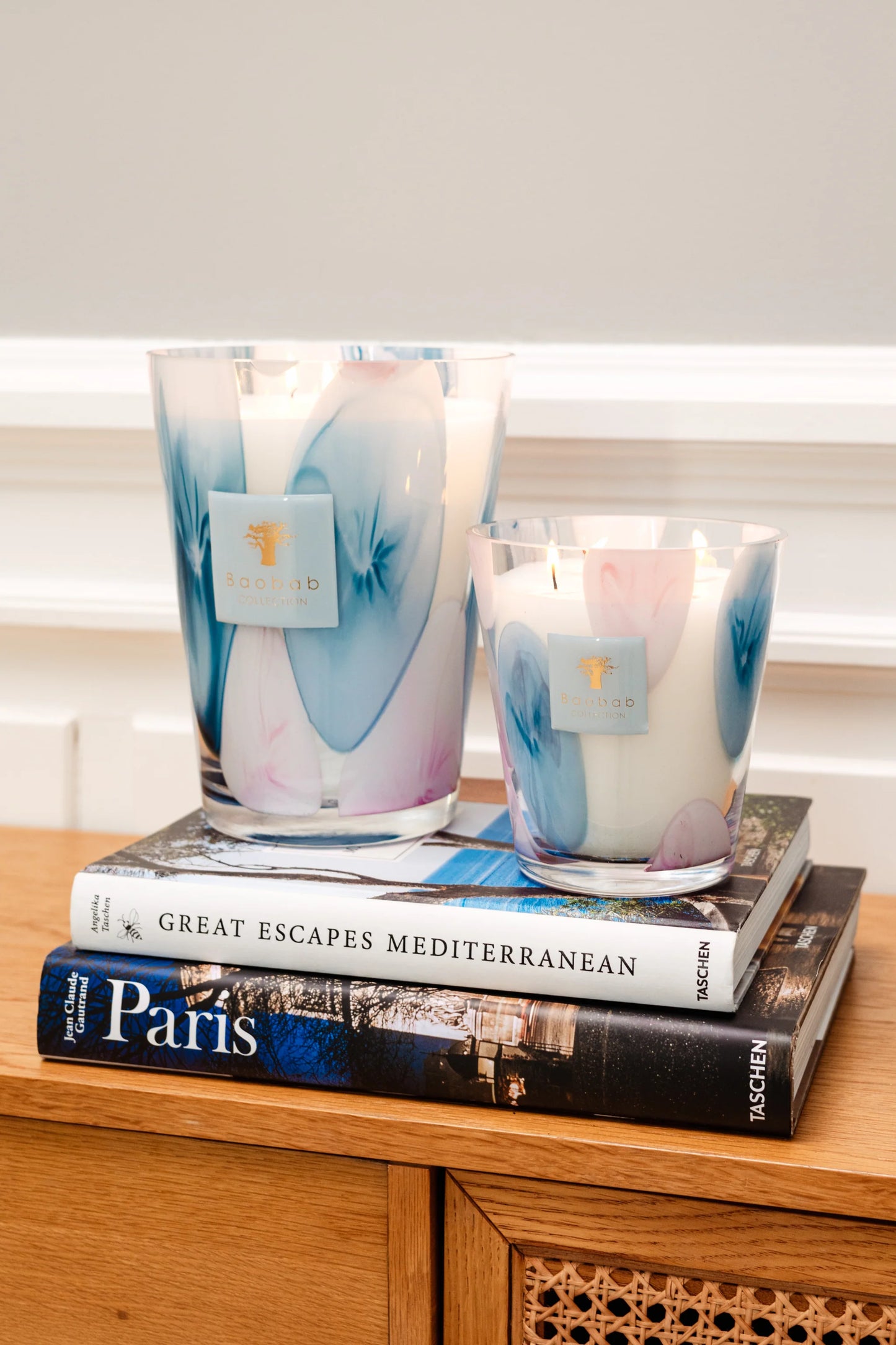 Baobab Collection scented candles in colorful glass on stacked books, adding a stylish touch to any decor.